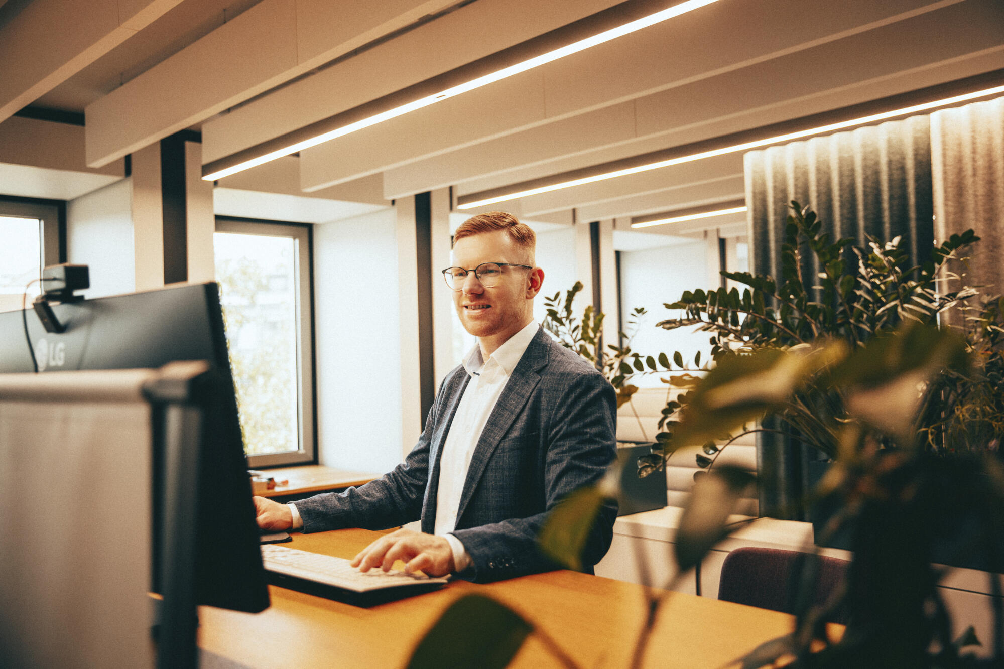 Carsten steht an seinem Arbeitsplatz, er tippt auf der Tastatur und schaut auf den Monitor.