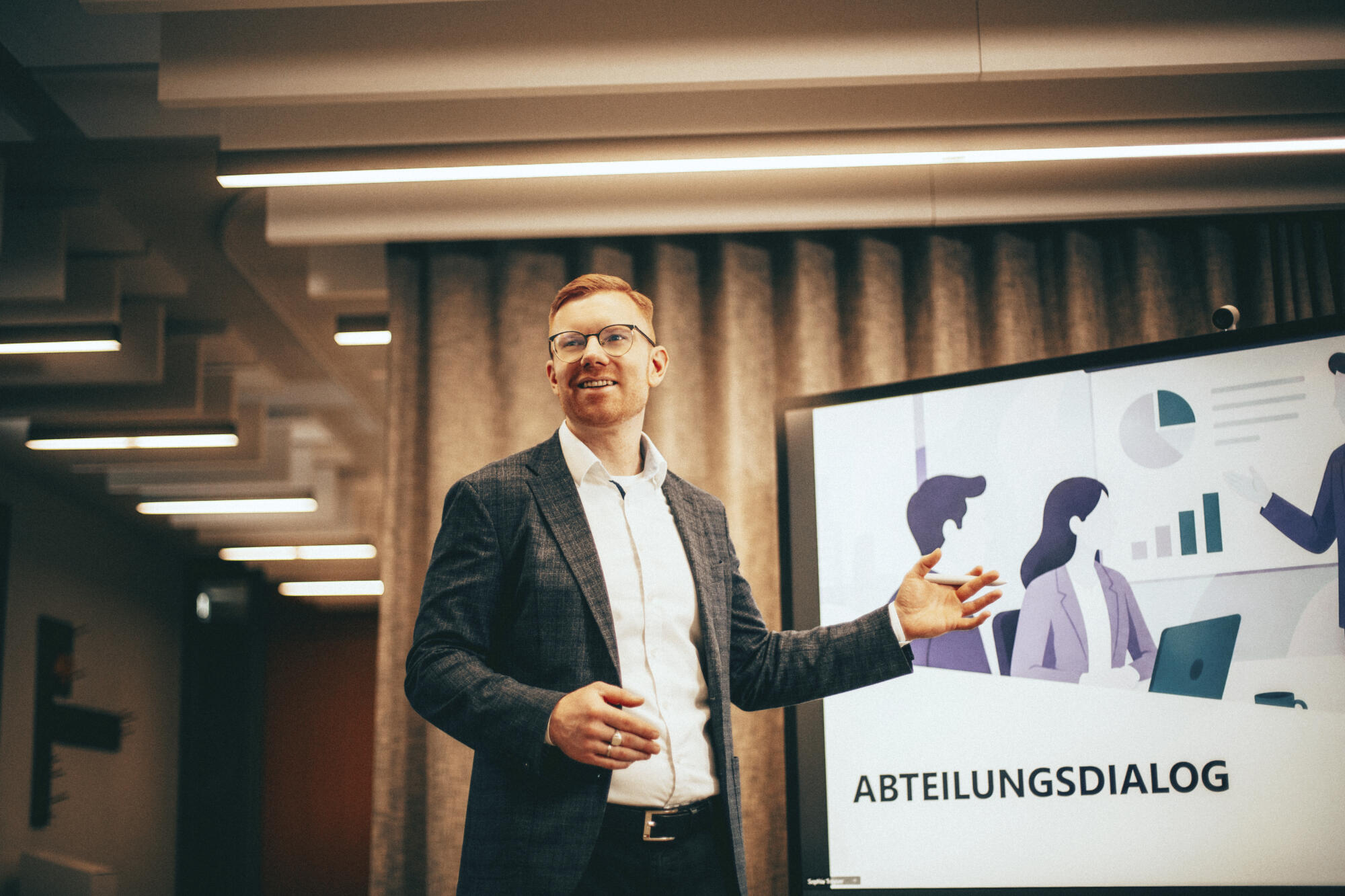 Carsten präsemtiert seinen Mitarbeitenden ein Thema. Man sieht nur Carsten wie er auf einen Monitor deutet.