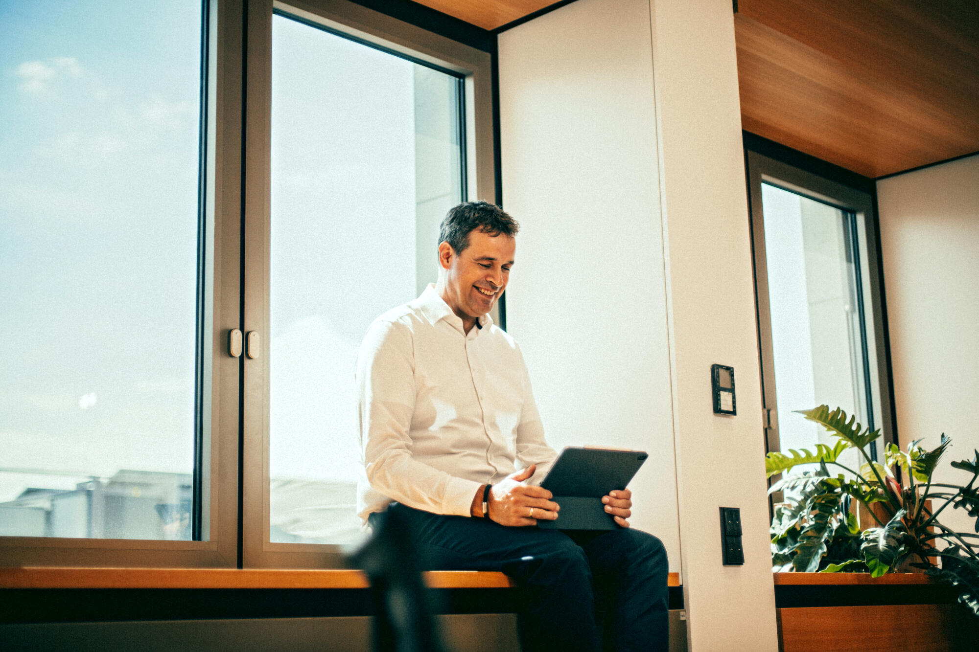 Ein Mitarbeiter sitzt auf einer Fensterbank und schau auf sein Tablet.