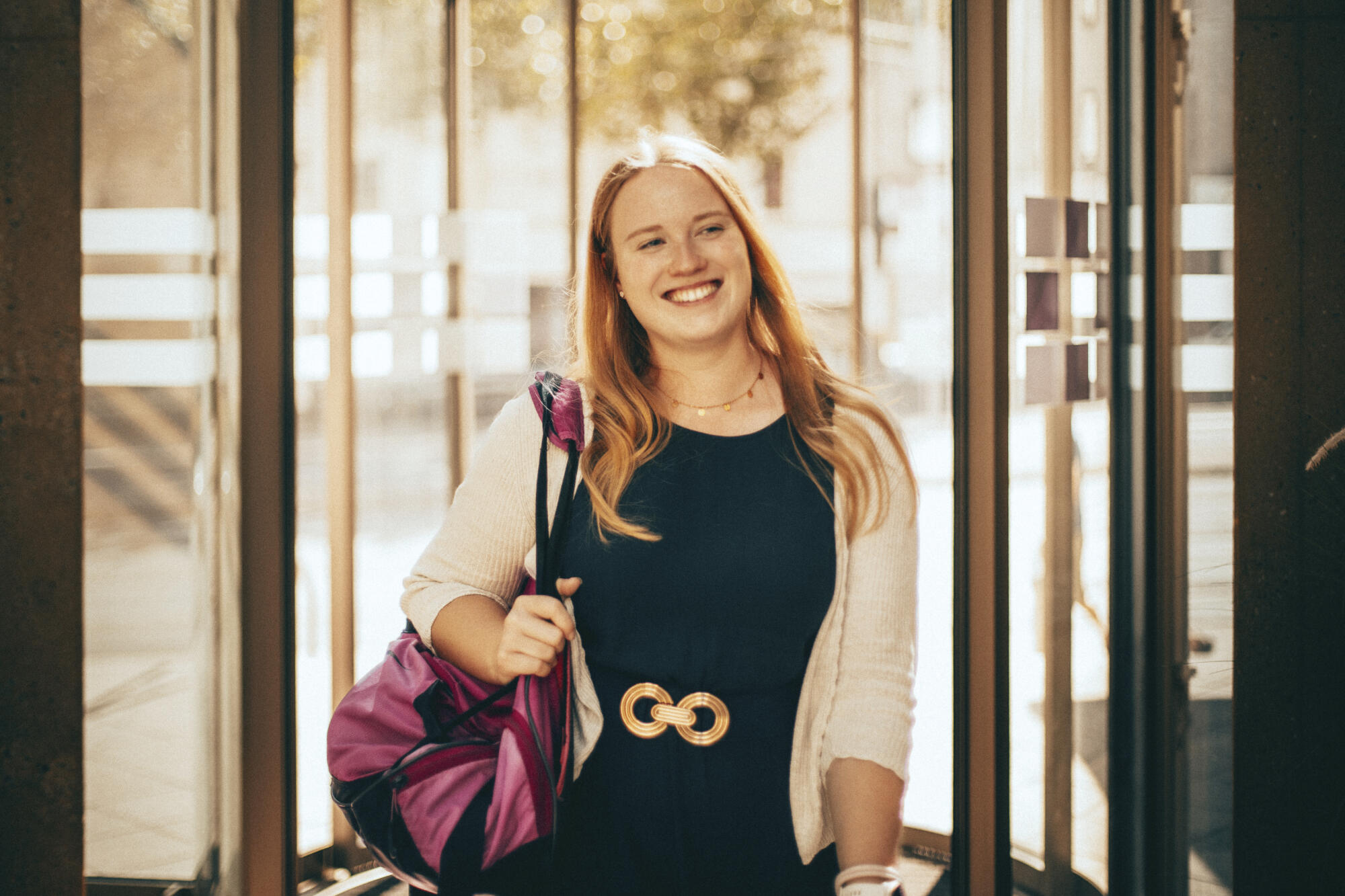 Lena trägt eine Sporttasche über der Schulter und kommt zum Eingang der Evangelischen rein. Sie lacht
