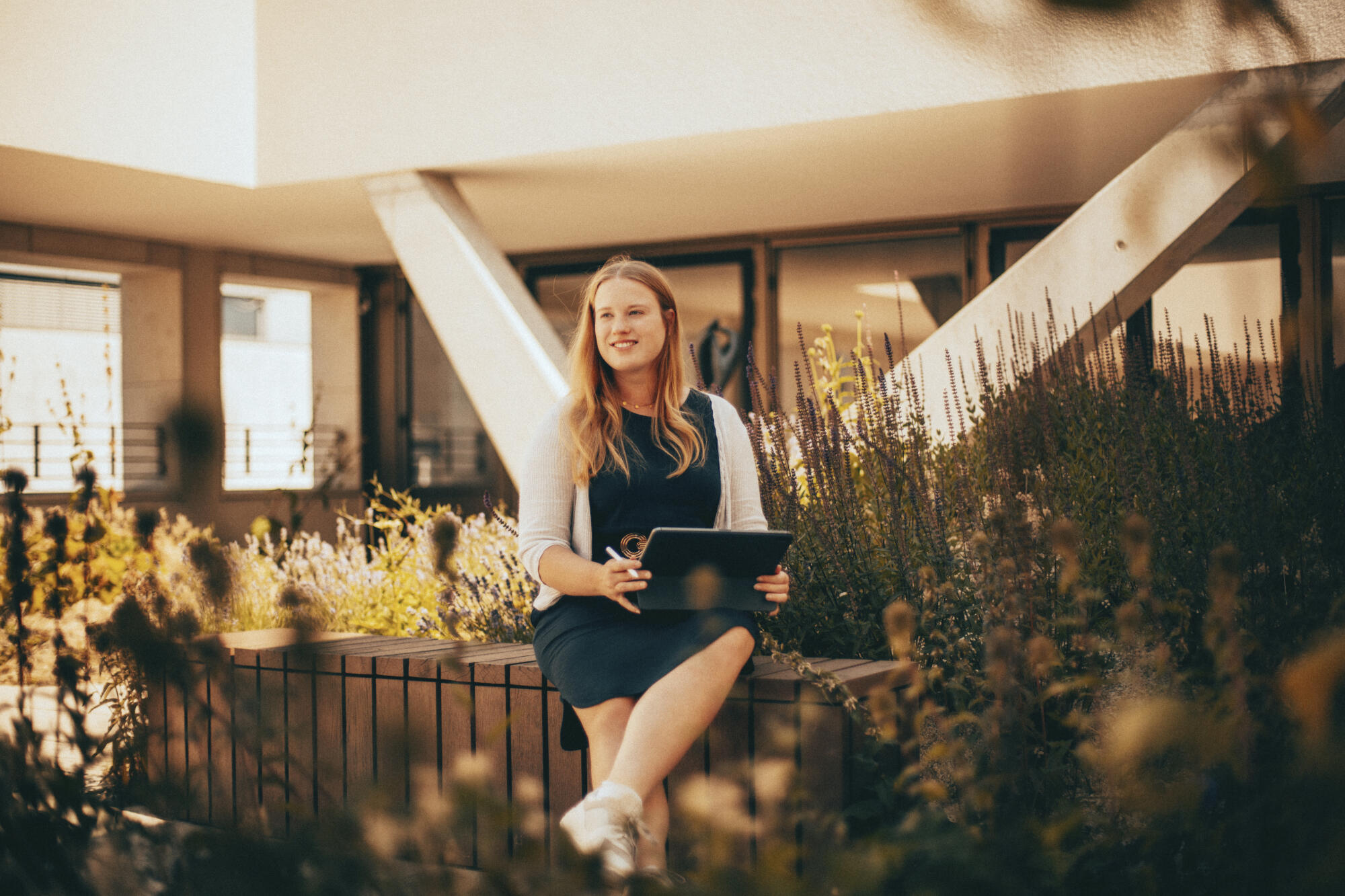 Lena Schöneweiß sitzt mit Tablet auf der Dachterrasse und denkt nach.