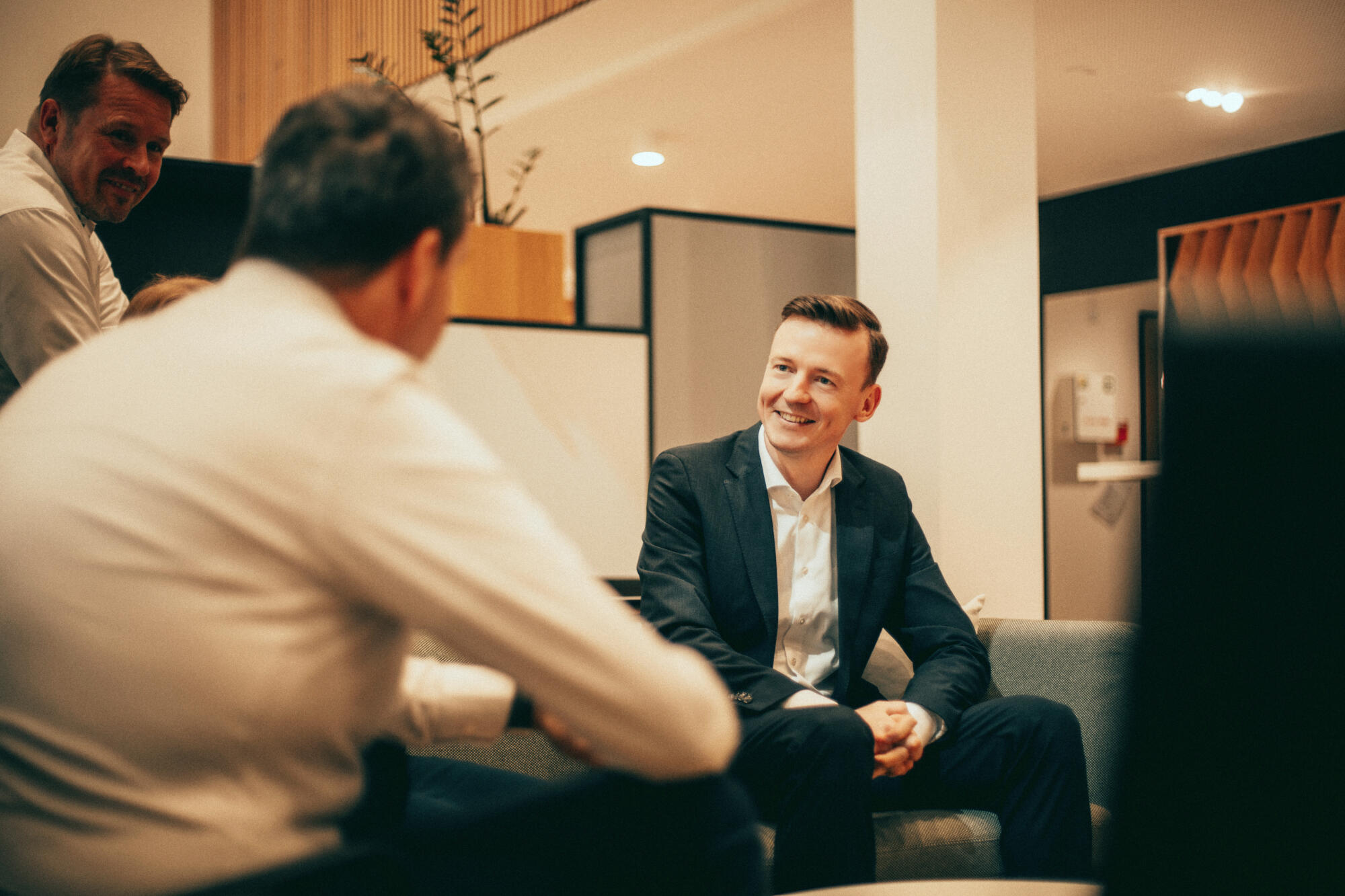 Ein junger Mann sitzt auf einem Sofa und lächelt seien Gesprächspartner an, der ihm gegenübersitzt.